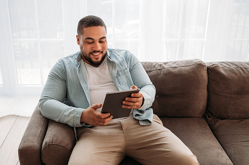 Smiling man with digital tablet sitting on a sofa at home