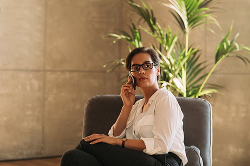 Portrait of a confident middle-aged businesswoman sitting on an armchair talking on a mobile phone