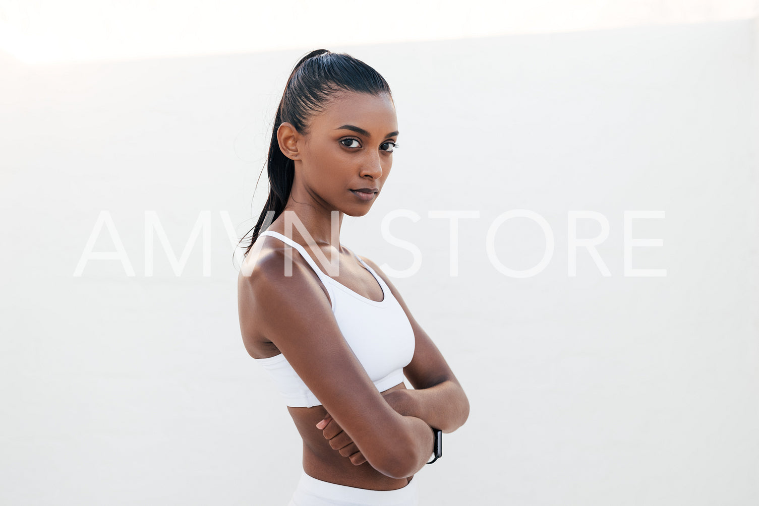 Confident athlete with crossed arms looking straight at a camera. Portrait of a slim and serious woman in white fitness clothes.