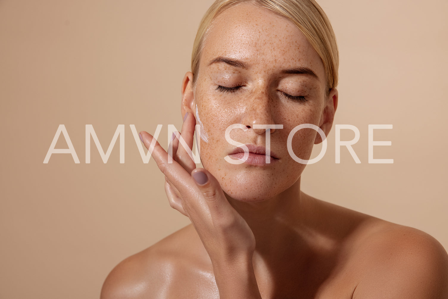 Beautiful female applying moisturizer on face in studio