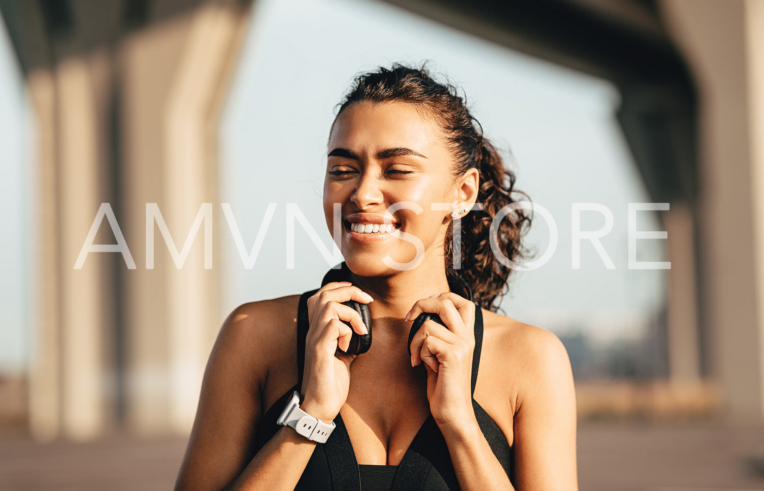 Happy woman relaxing after training standing outdoors and holding headphones	