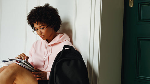 Young African American girl studying indoors, sitting at wall