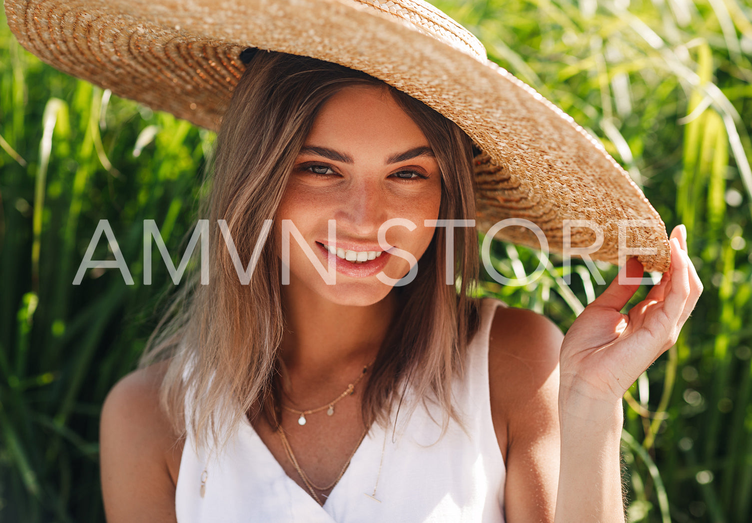 Beautiful blond woman in straw hat looking at camera and smiling while sitting outdoors	