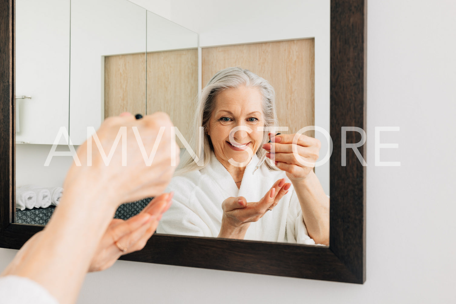 Senior woman in the bathroom doing morning routine. Female holding dropper with hyaluronic acid in front of a mirror.