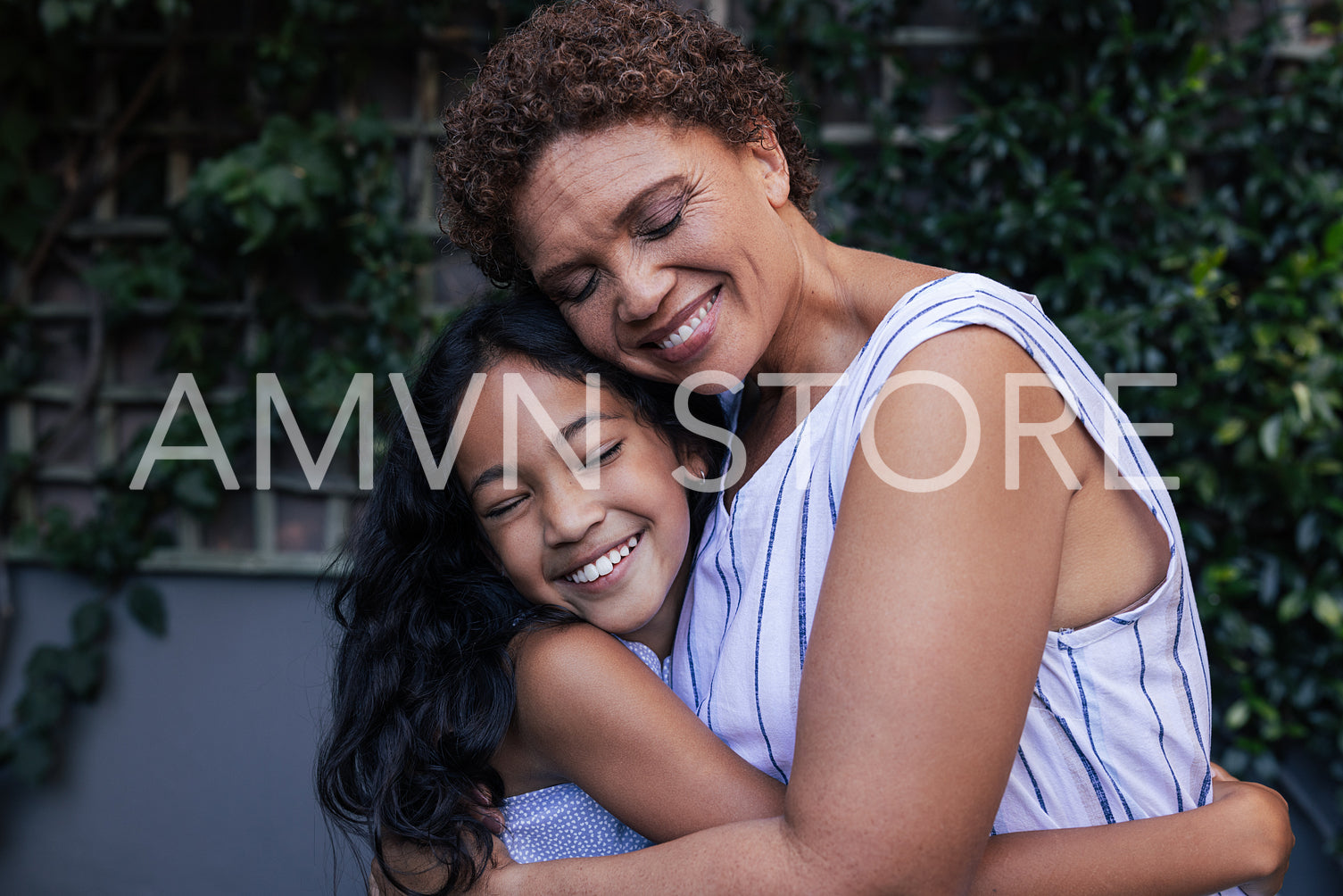 Granny and kid hugging. Happy grandma and granddaughter embracing with closed eyes at backyard.