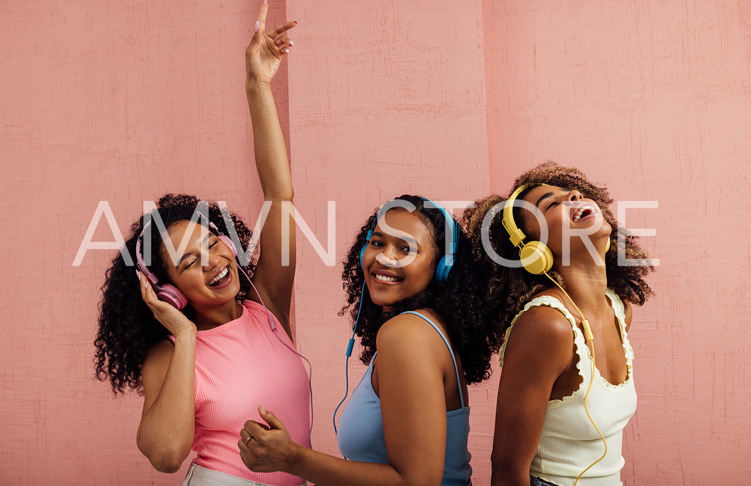 Three young women with curly hair wearing headphones and dancing