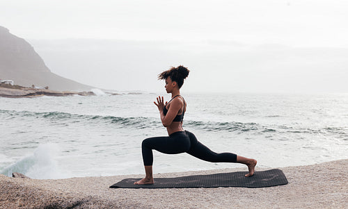 Side view of female practicing yoga on a mat by the ocean in the evening