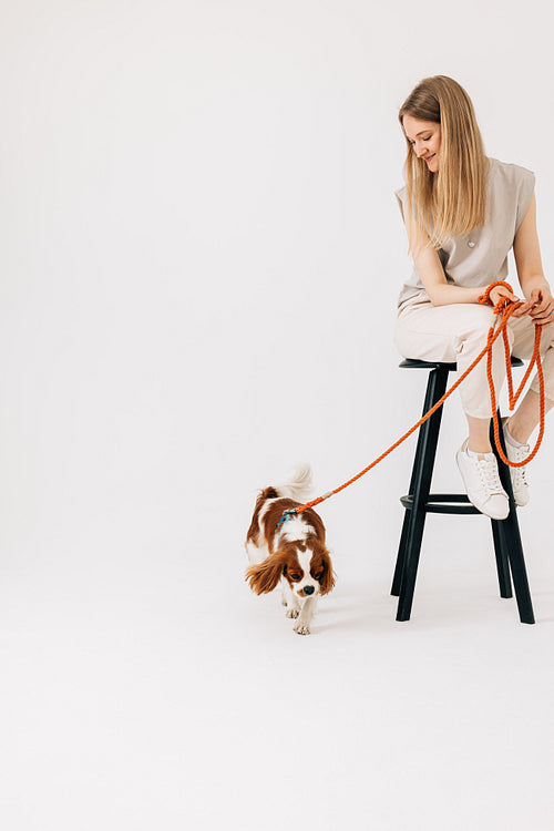 Young woman sitting on chair with dog leash and pet