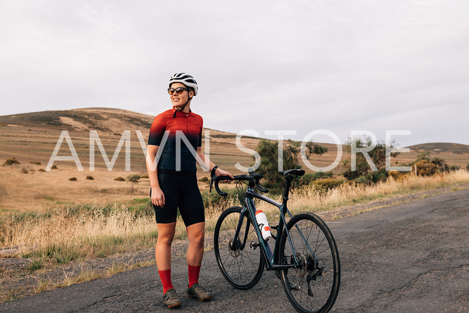 Female cyclist taking break from riding bike standing on empty road