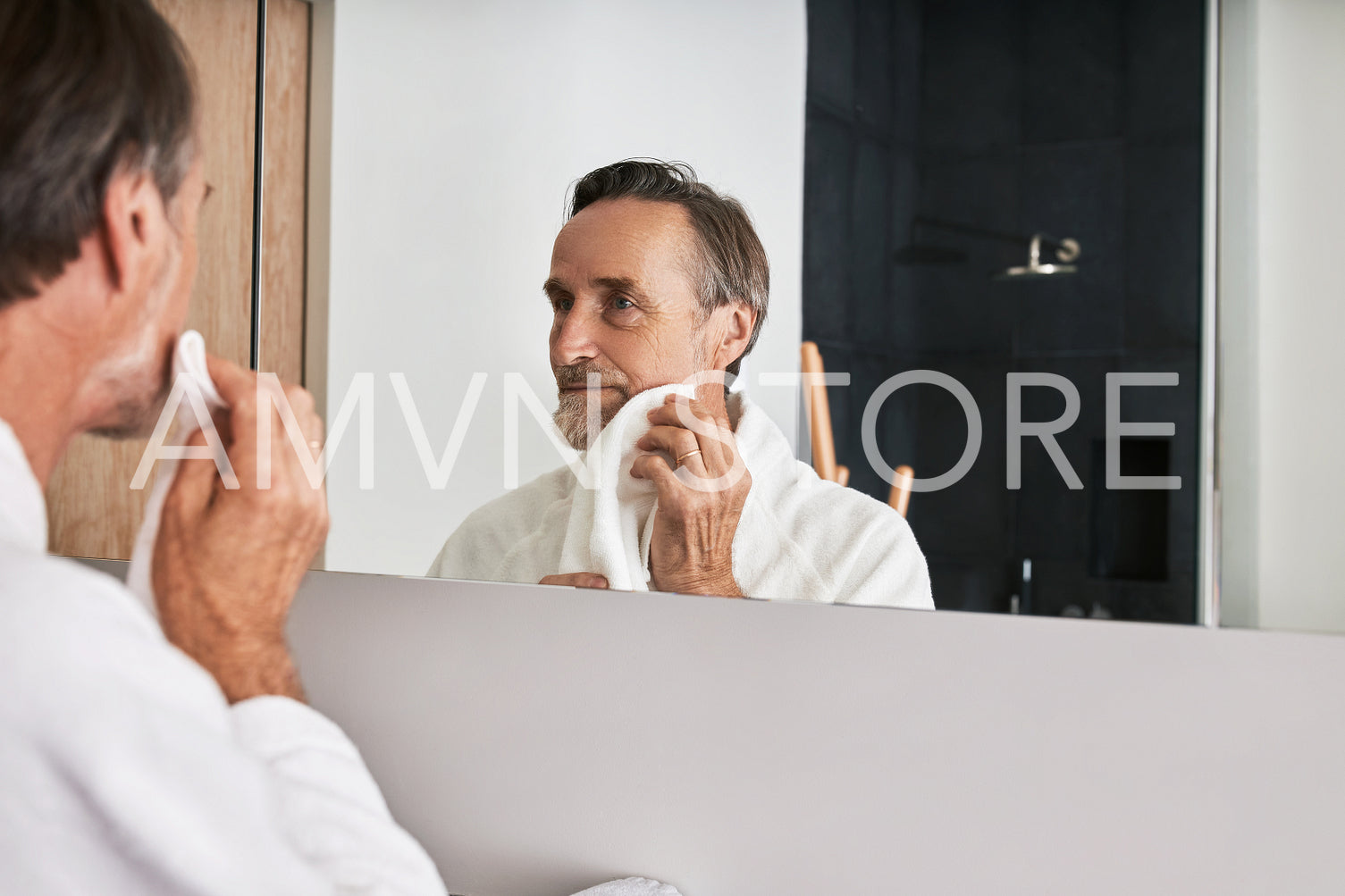 Handsome mature man wiping his cheek with a towel in a bathroom in front of a mirror	