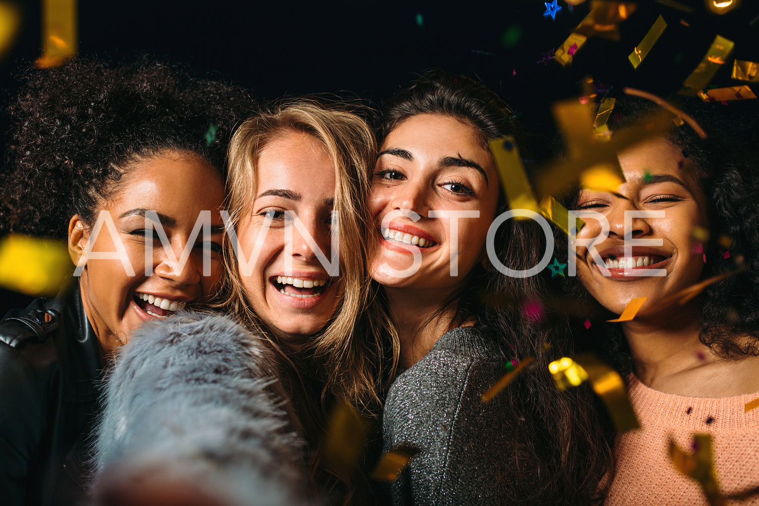 Four happy women taking selfie under golden confetti at night