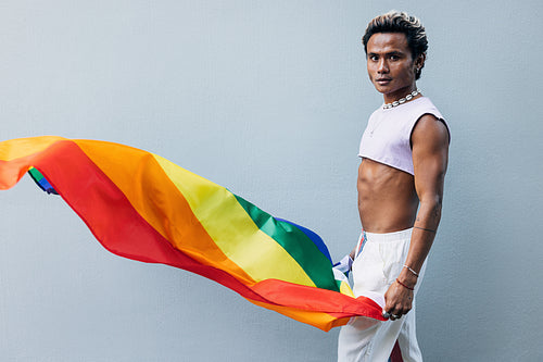 Handsome male with rainbow flag looking at camera at grey wall