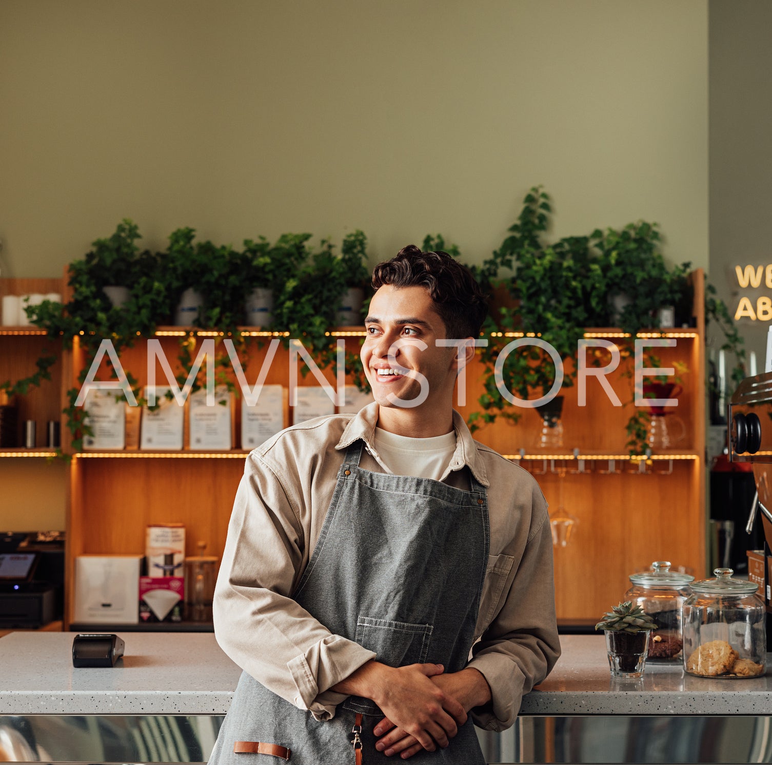 Portrait of a handsome coffee shop owner looking away. Young male in an apron leaning counter.