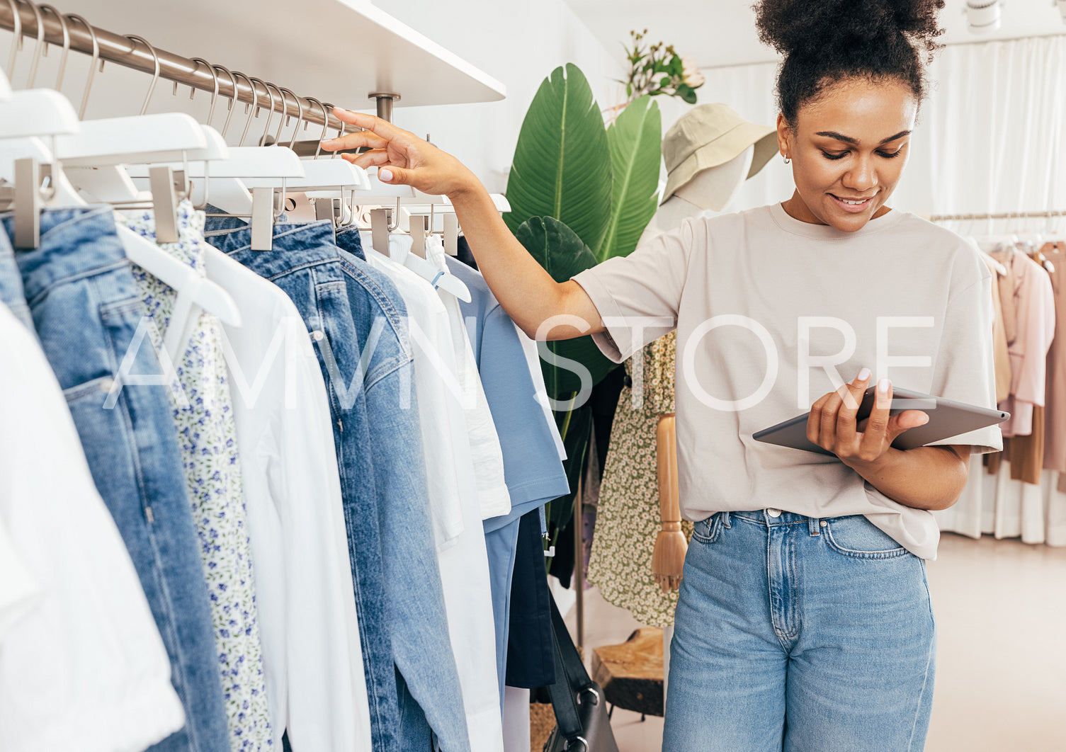 Young boutique owner taking inventory standing at rack with digital tablet