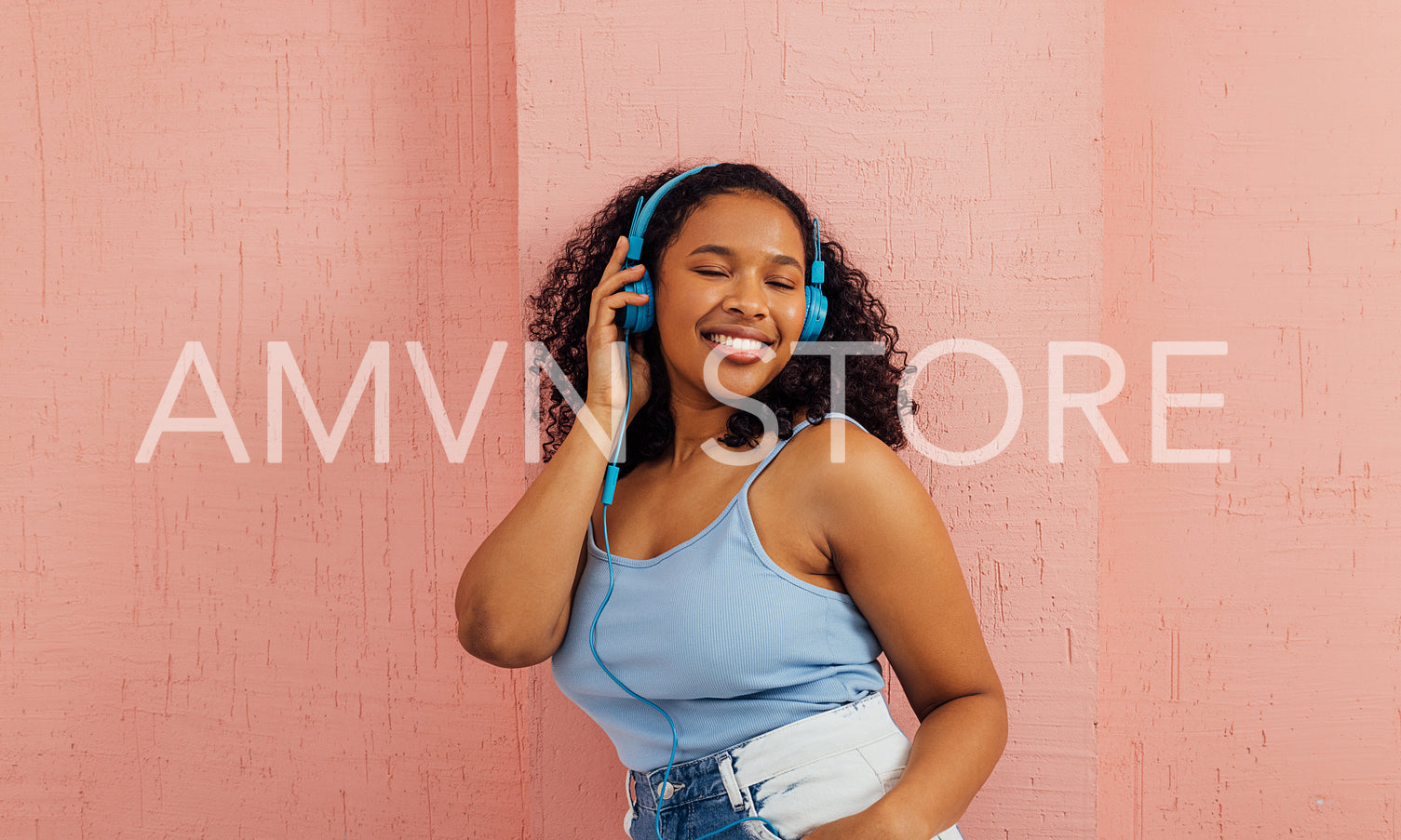 Young cheerful woman enjoying music with closed eyes at pink wall