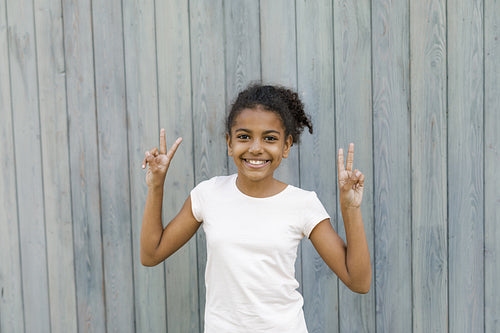 Happy girl standing at wall outdoors, making the victory sign with her hands