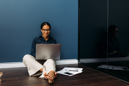 Smiling entrepreneur sitting on the floor at home with a laptop on her legs