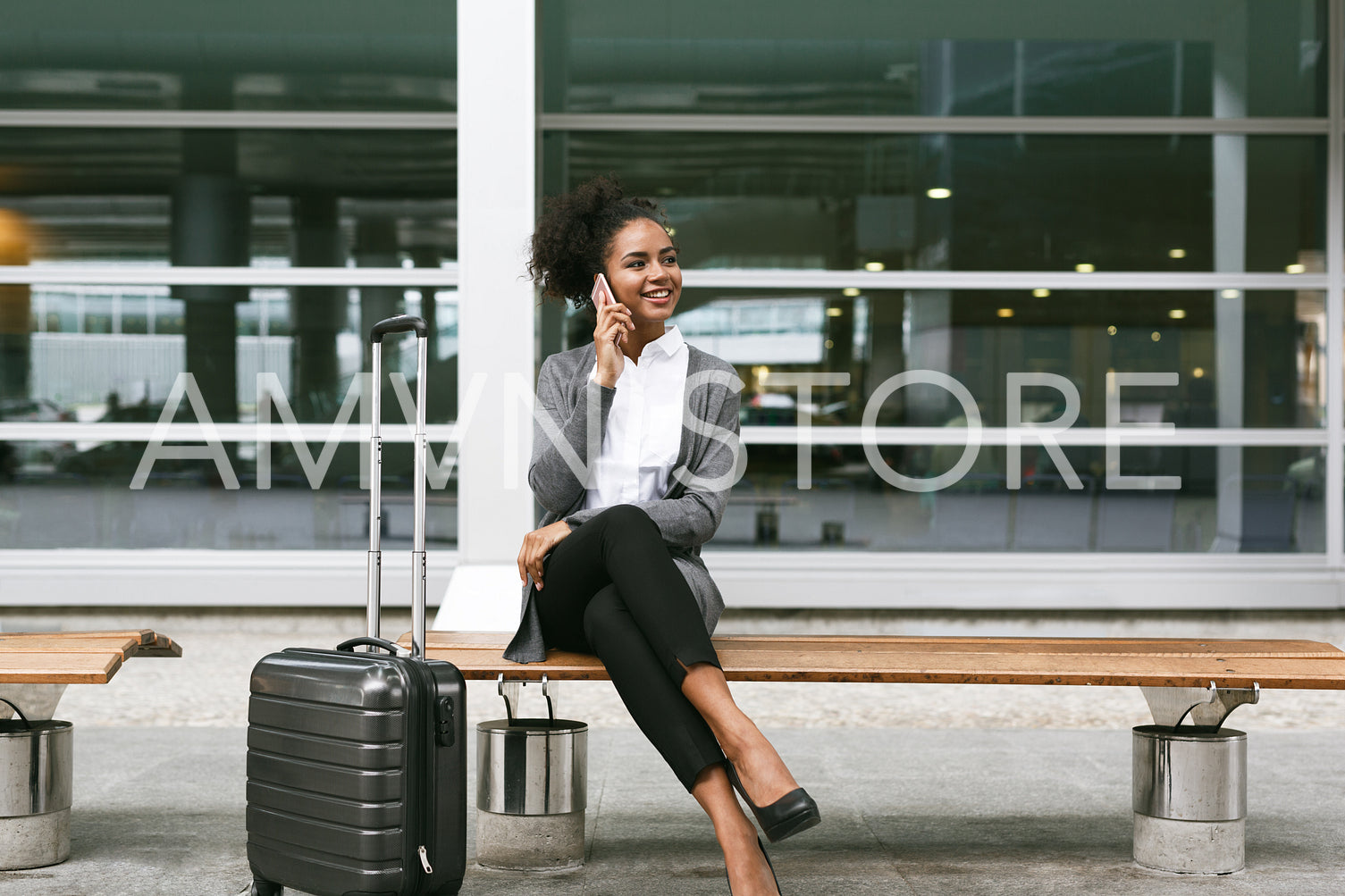 Smiling businesswoman sitting on bench and talking on mobile phone at airport terminal	