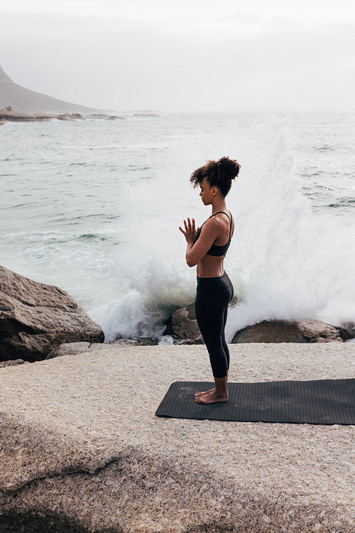 Full length of slim woman meditating against the waves. Side view of young female practicing yoga outdoor by ocean.