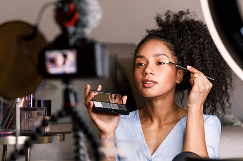 Female video blogger applying make up on face in living room