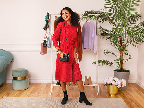 Personal stylist wearing red dress in studio. Woman posing at clothes rack.