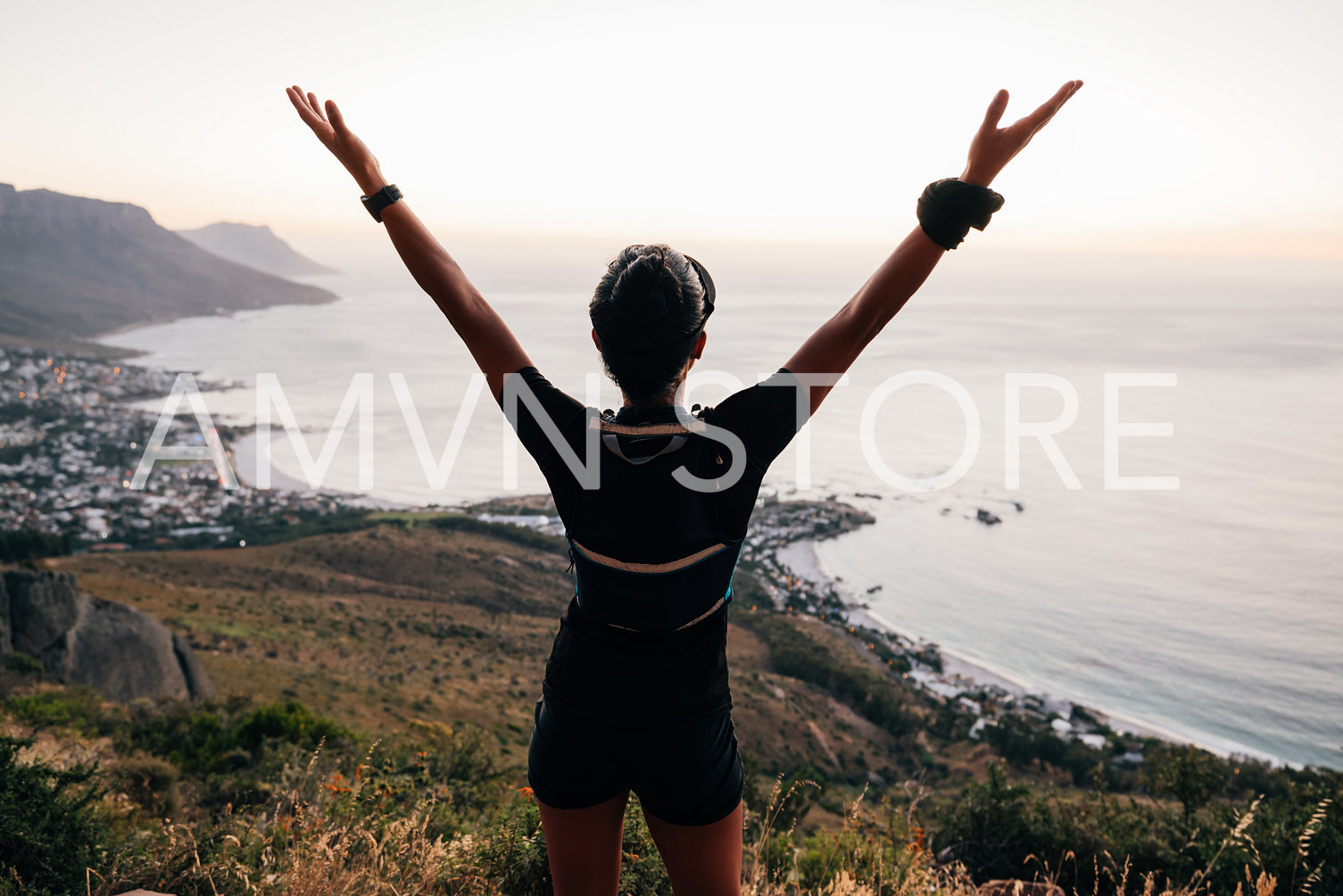 Rear view of trail runner enjoying sunset. Woman in sportswear raising hands while looking at scenic view.