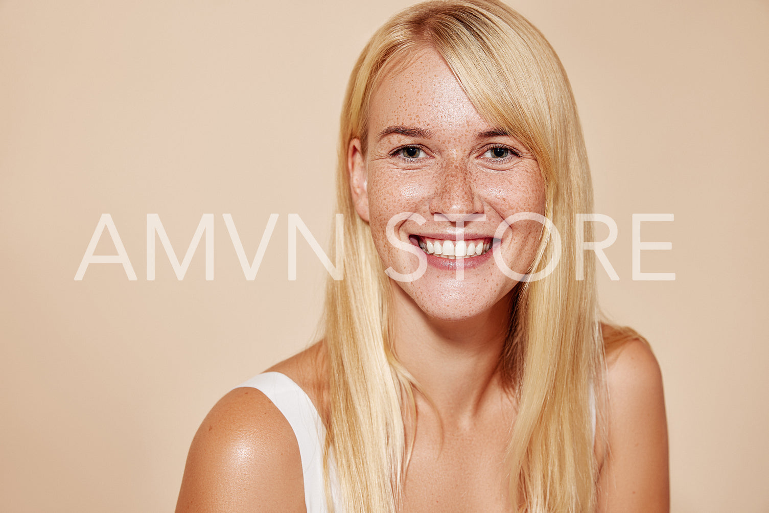 Cheerful blond female with perfect smooth skin looking at camera. Portrait of a happy freckled woman looking straight at a camera.