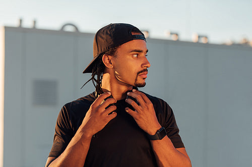 Young male athlete with dreadlock wearing a black hat looking away