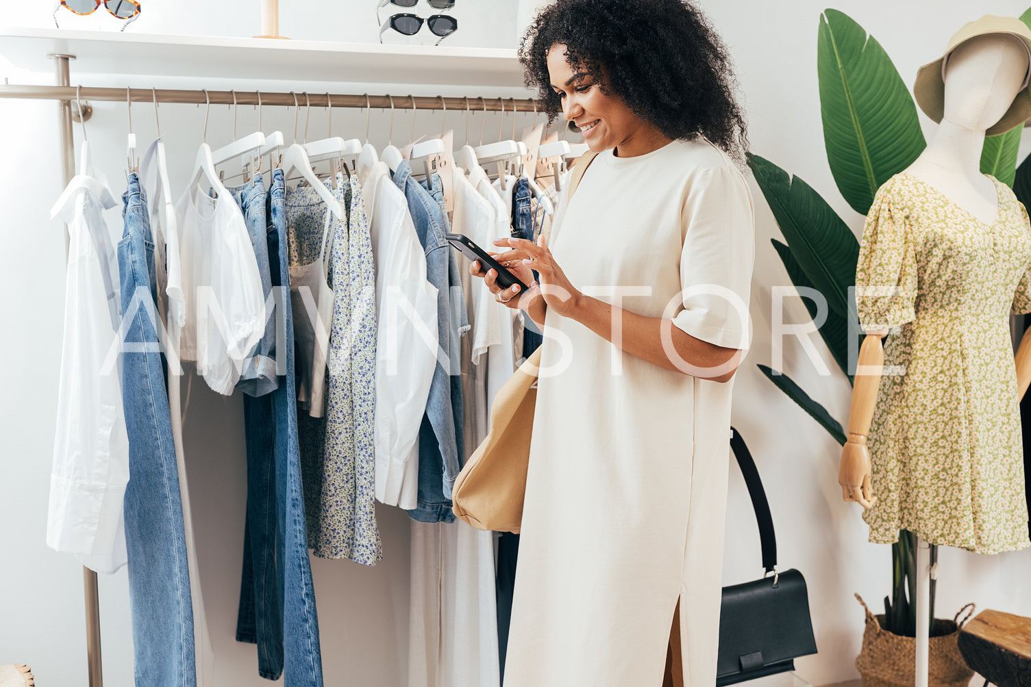 Side view of a young stylish woman holding a mobile phone at rack in small boutique