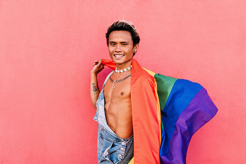 Happy male wearing overalls holding LGBT flag and looking at camera