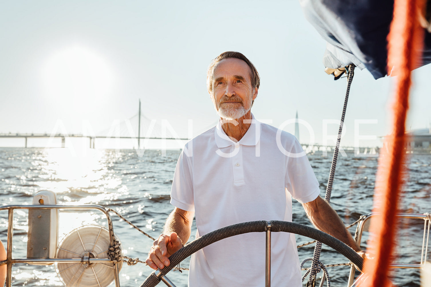 Mature man steering a private yacht while on vacation. Bearded yachtsman standing on his sailing boat looking at distance.	