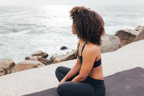 Woman with curly hair looking at ocean while relaxing after yoga exercises