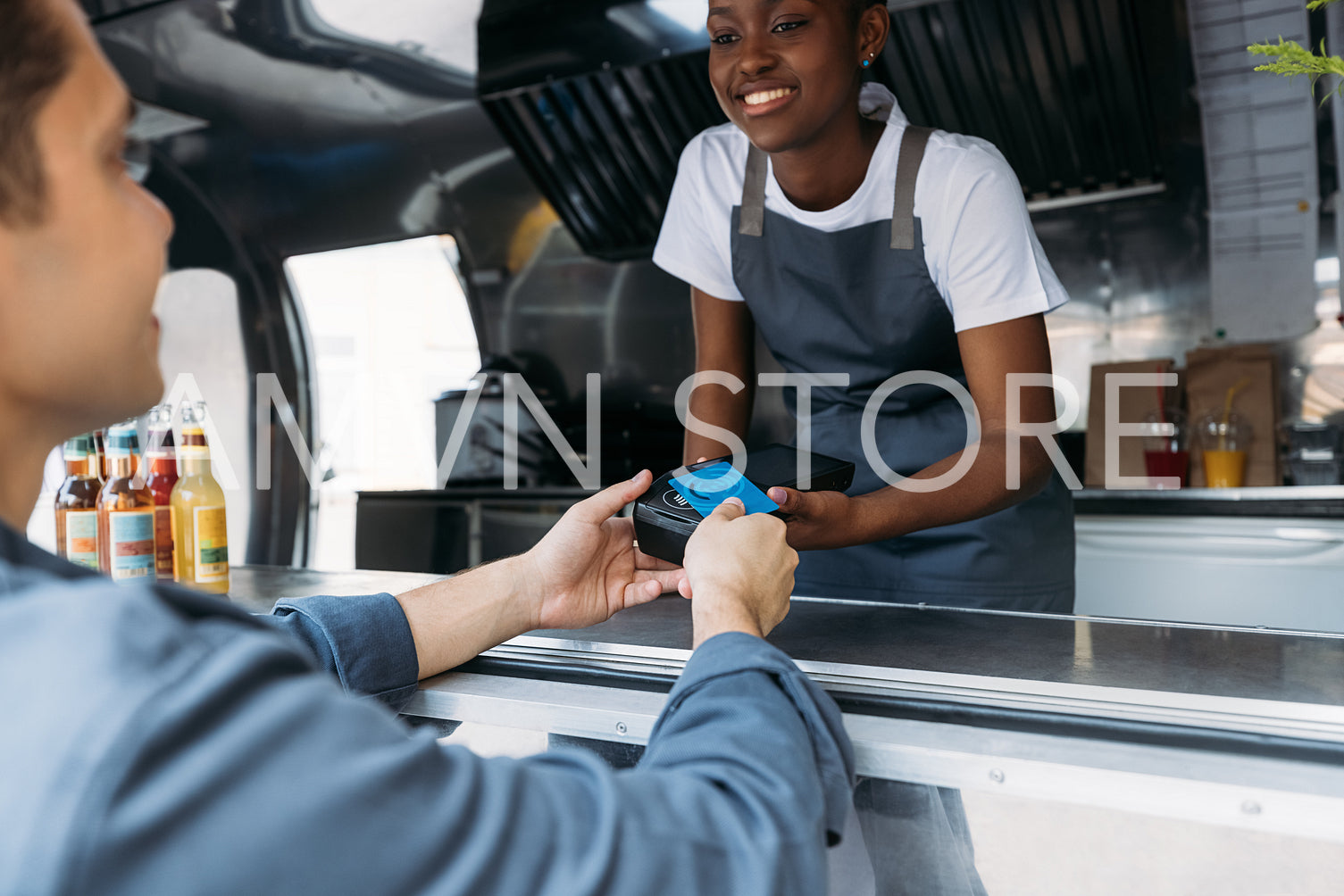 Customer paying with a credit card at a food truck. Smiling saleswoman in apron holding a pos terminal while buyer making NFC transaction.