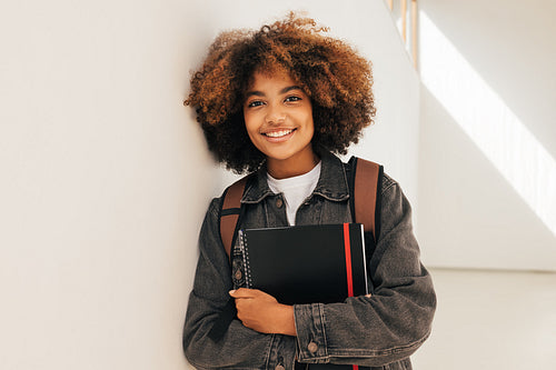 Portrait of a young beautiful female student leaning a wall. Smiling girl looking at camera while standing in high school.