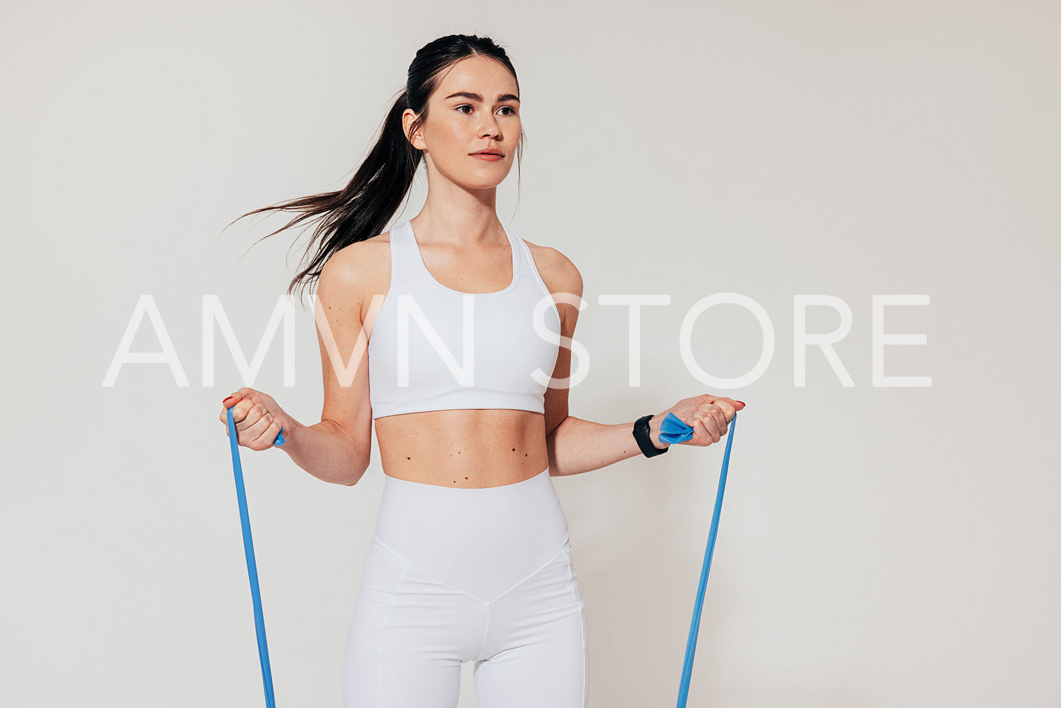 Fit woman in white sports clothes exercising with resistance band in studio