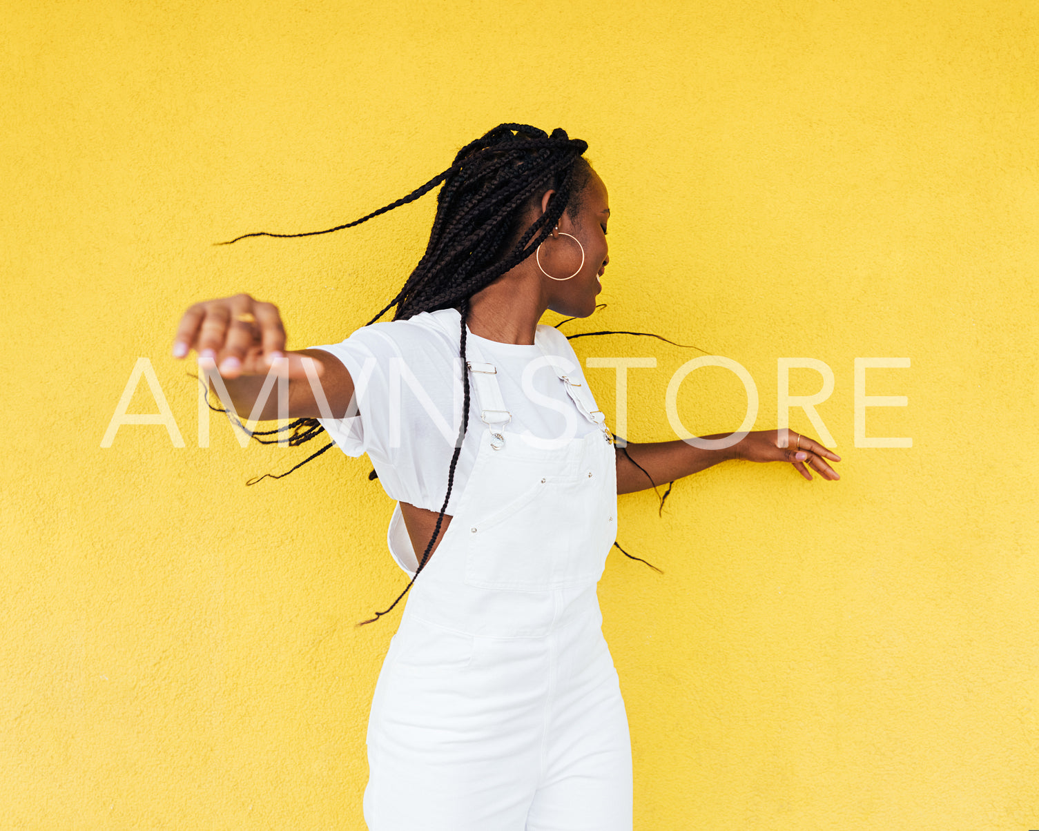 Young woman in white overall having fun against a yellow wall outdoors