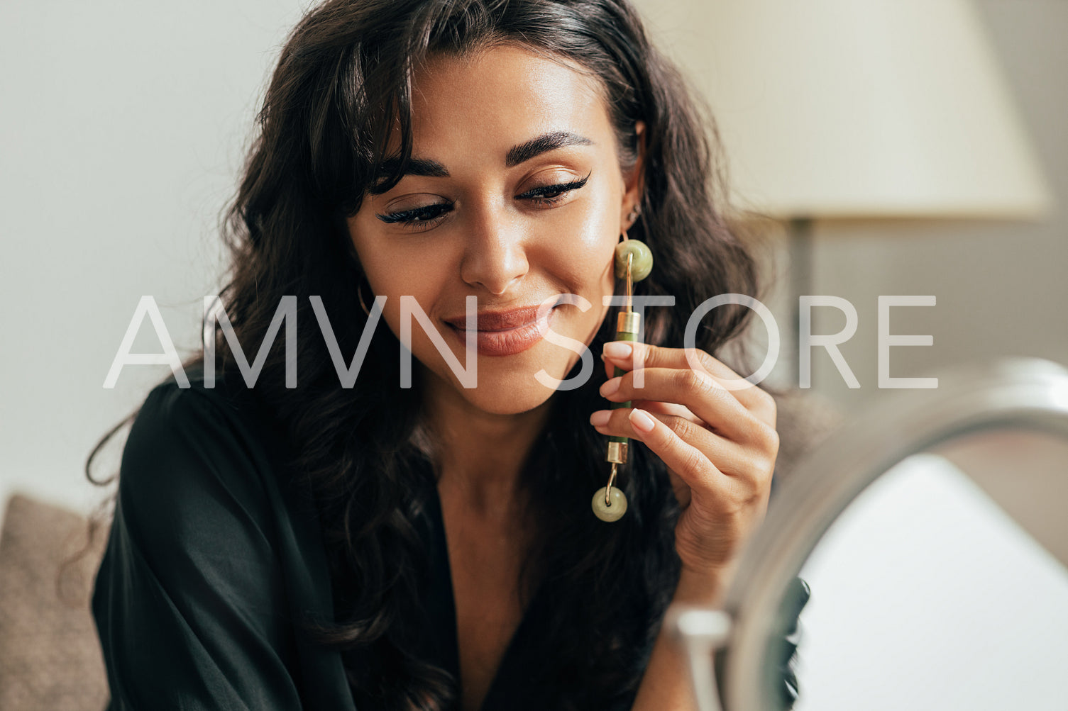 Close up of woman massaging face with jade roller while sitting in front of a mirror