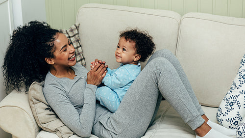 Mother playing with baby boy lying on sofa