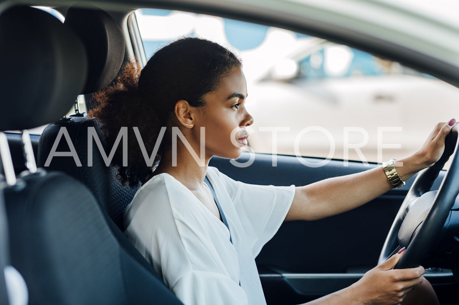 Side view of a woman sitting in a car holding a steering wheel and looking on the road	