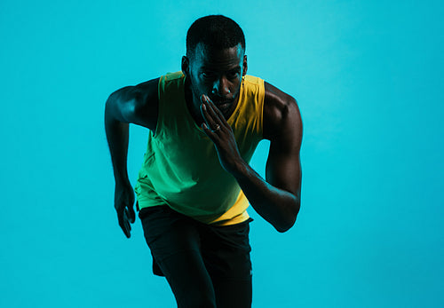 Portrait of an athlete against a blue background in position to start a run