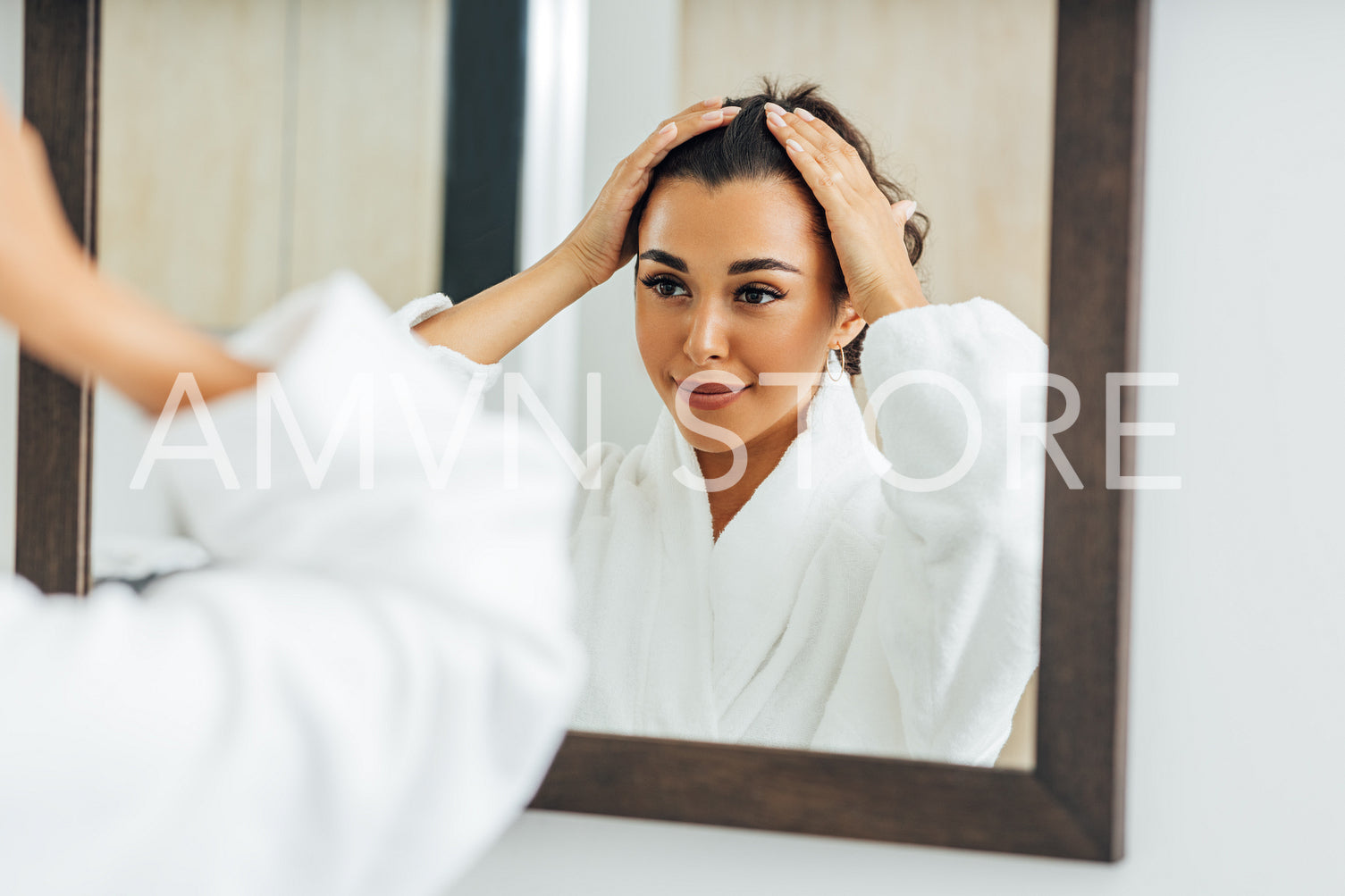 Beautiful middle east woman wearing bathrobe adjusting her hair in front of a mirror	