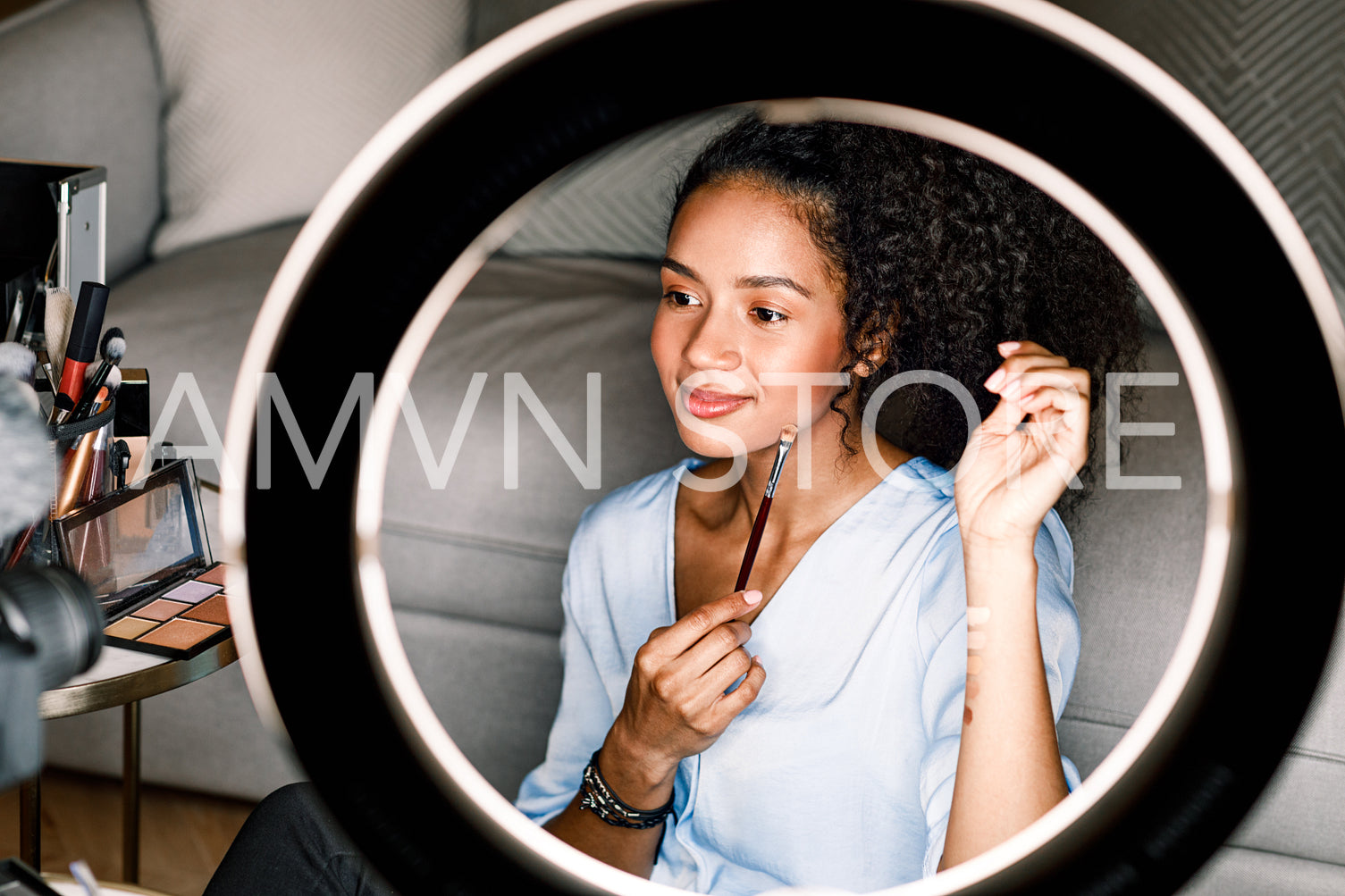 Makeup artist recording video from home. Woman applying cosmetics sitting in front of ring light.