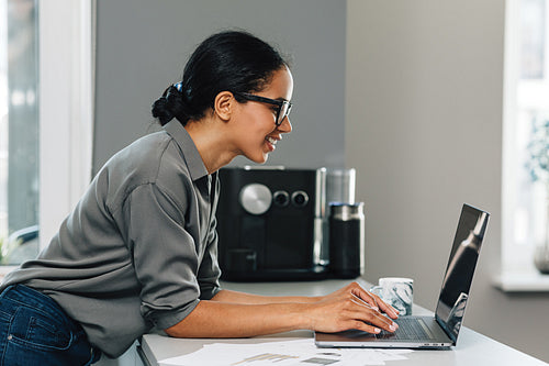 Side view of a young woman working from her kitchen, typing on laptop