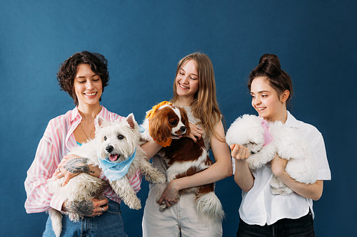 Three smiling pet owners holding their little cute dogs while st