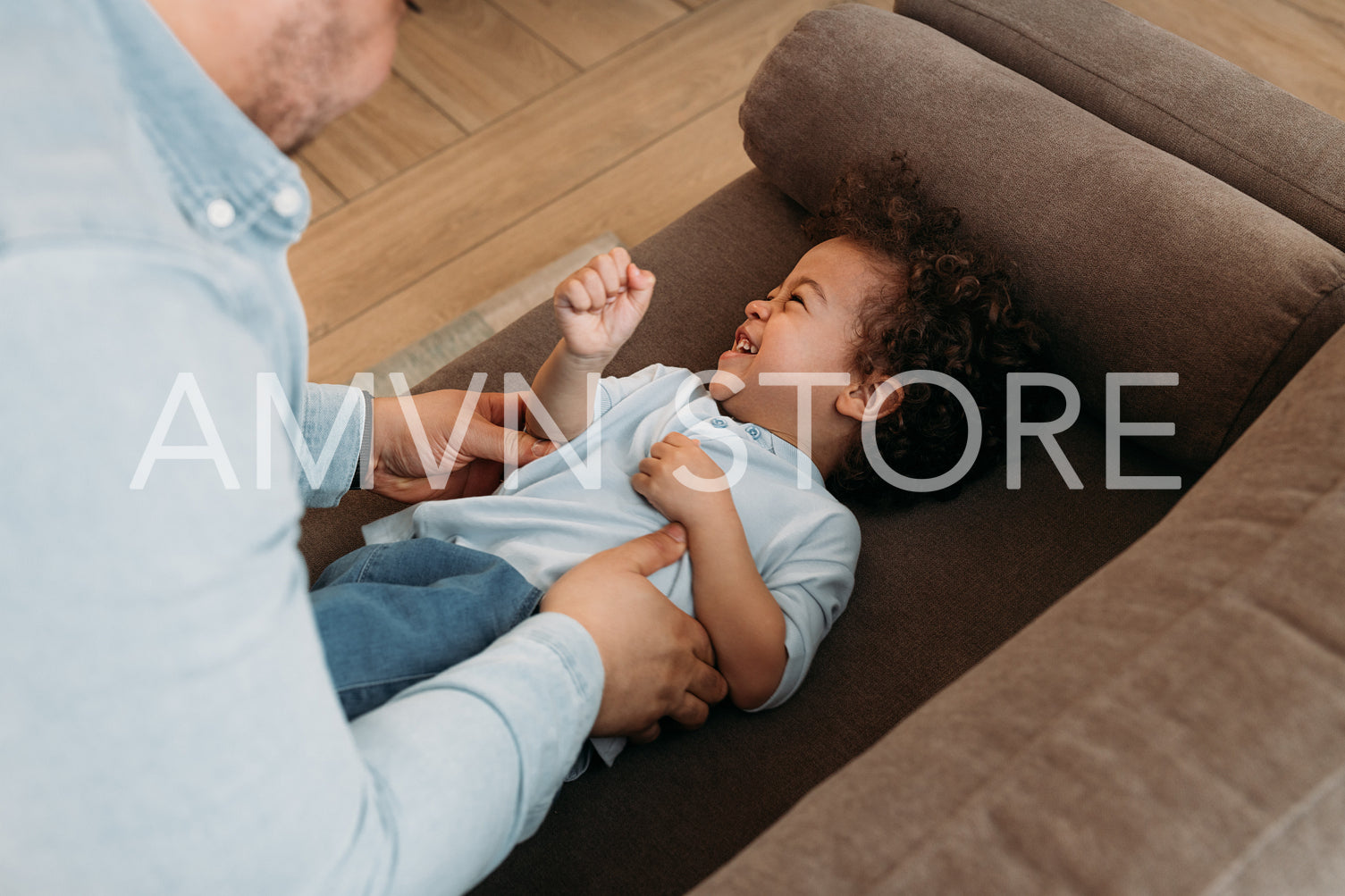 Little boy lying on sofa and laughing while father tickling him	