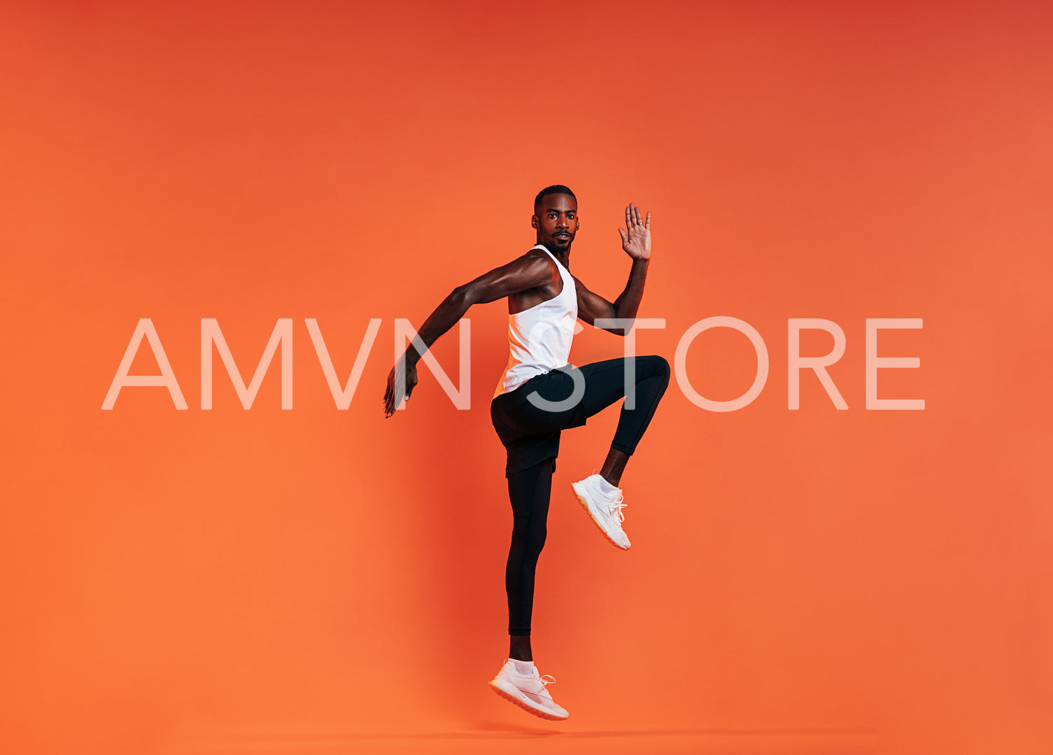 Young fit man doing exercises in studio. Male athlete jumping in the air over an orange background.