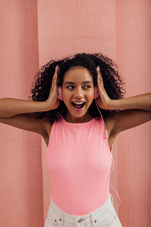 Surprised woman with curly hair touching headphones and looking away