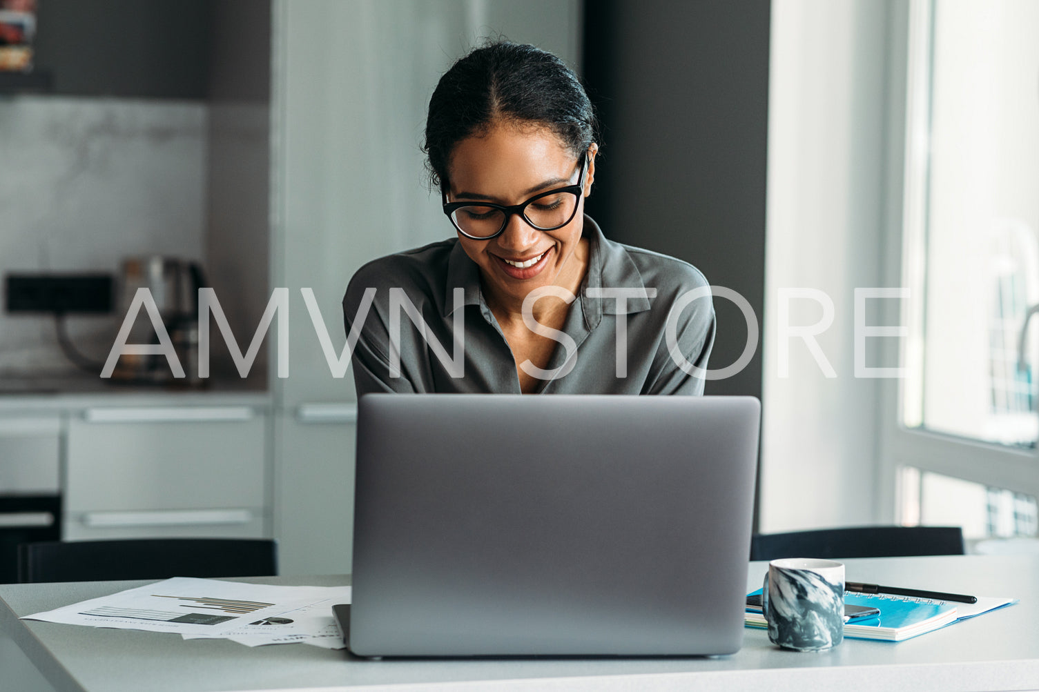 Smiling woman standing at the kitchen counter and working on a laptop computer from home	