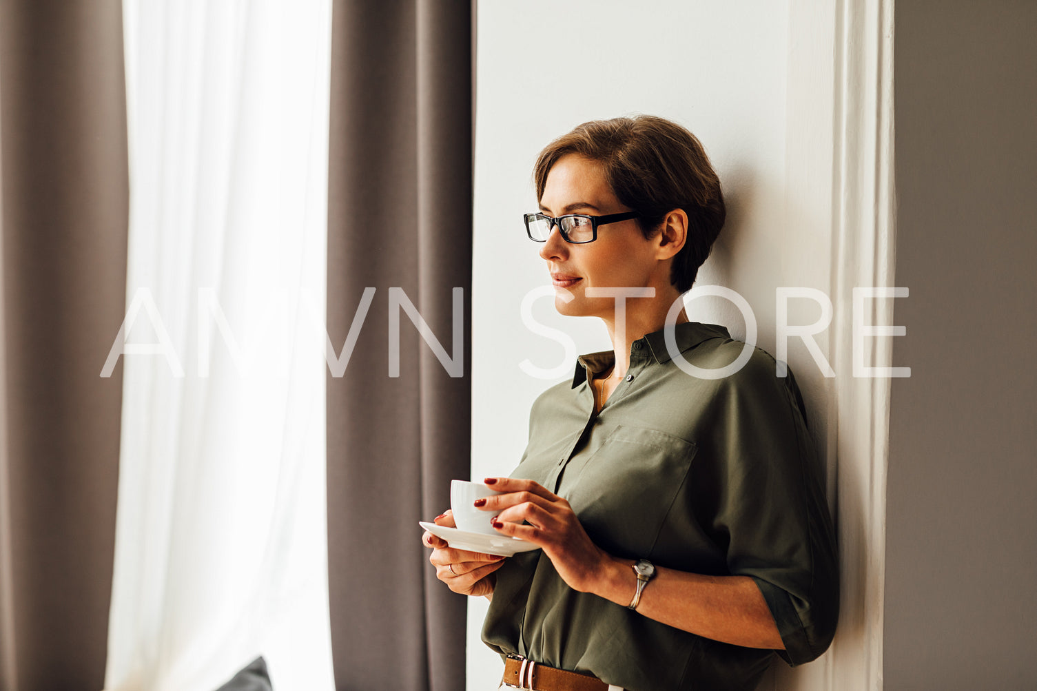 Mid adult caucasian woman in formal clothes standing in apartment room and having a cup of coffee	