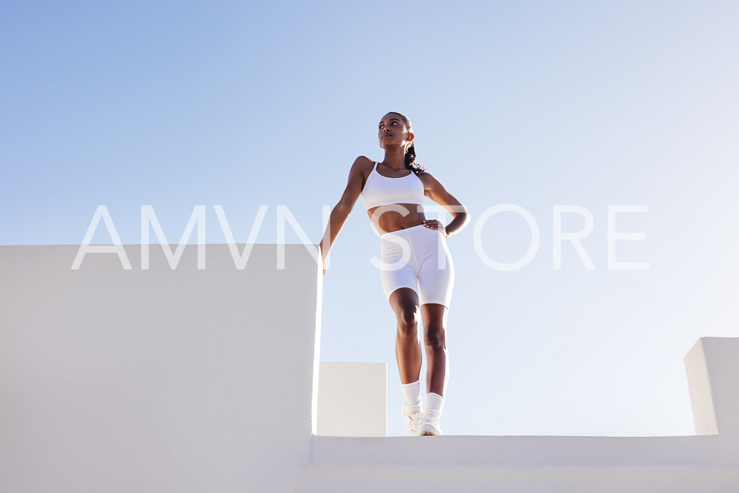 Beautiful sportswoman posing while standing outdoors against the skies. Full length of a young female in white sports clothes taking a break.